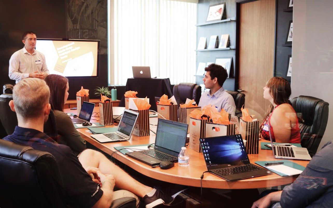 Colleagues in a workshop seated around a conference table with laptops